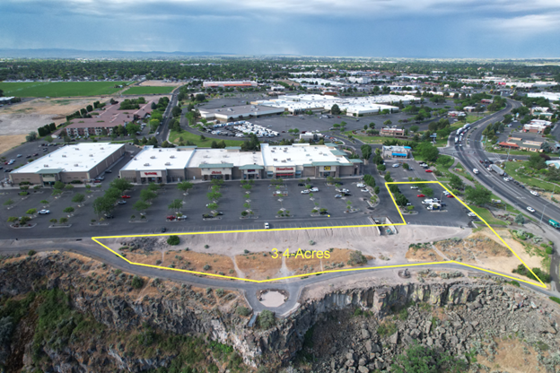 Aerial view of a commercial area beside a rocky cliff, with parking lots, buildings, and roads.