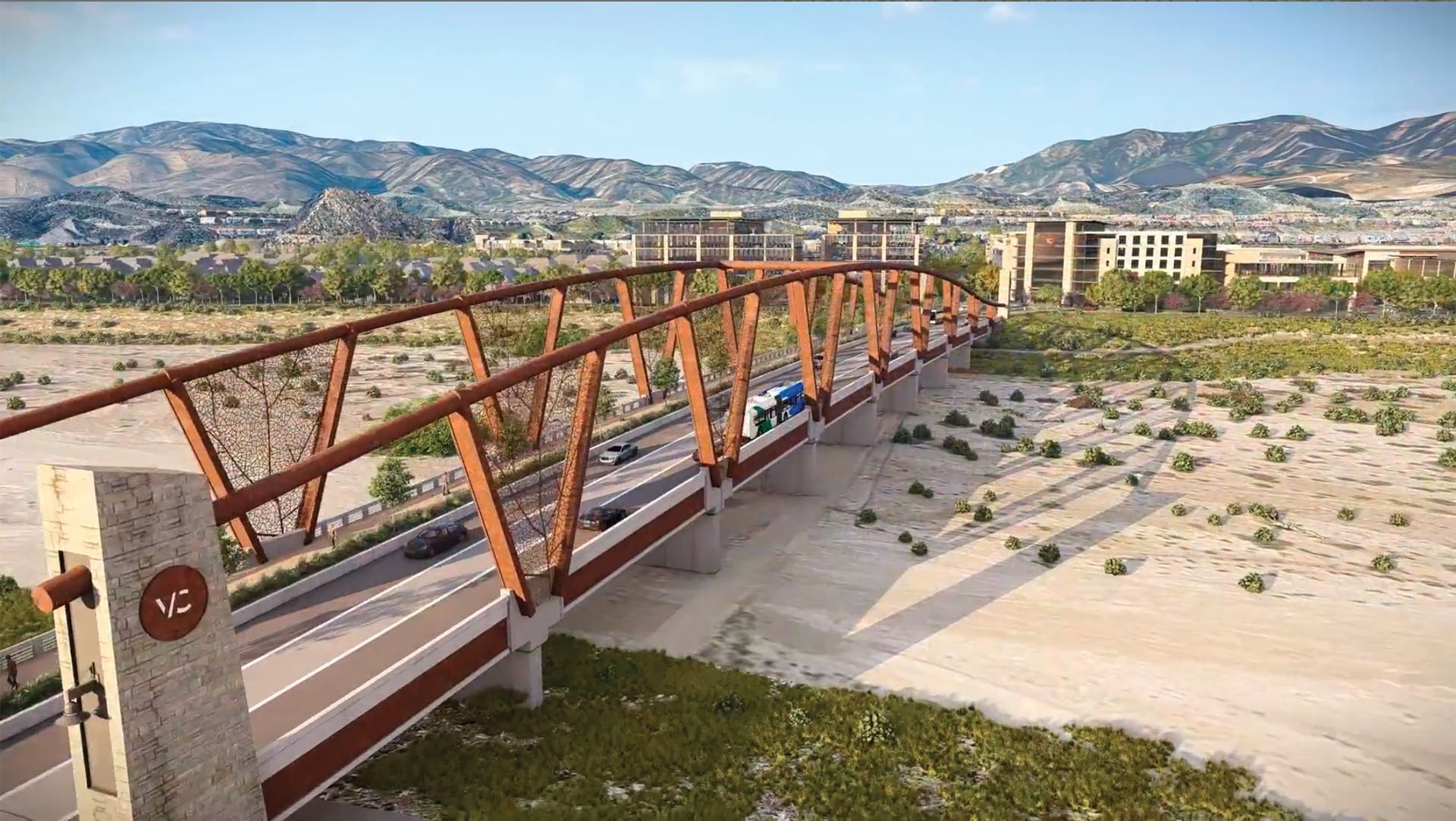 Orange bridge over a dry riverbed with mountains and buildings in the distance