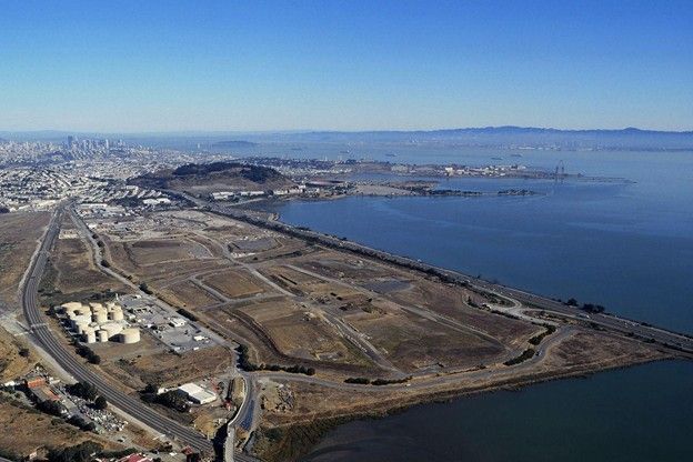 Aerial view of a coastal industrial area beside a bay, with docks, roads, and open land