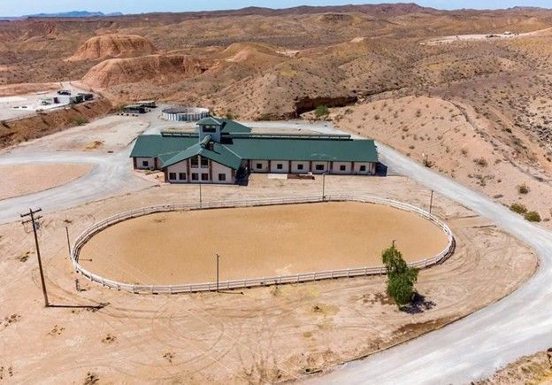 Aerial view of a desert ranch with a green-roofed building and oval dirt corral