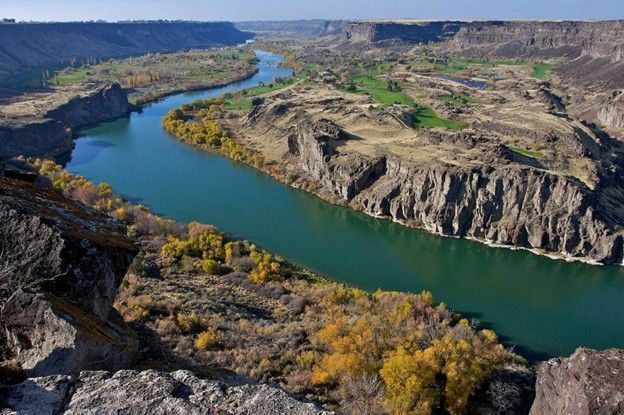 Winding blue river through a rugged canyon with rocky cliffs and autumn trees
