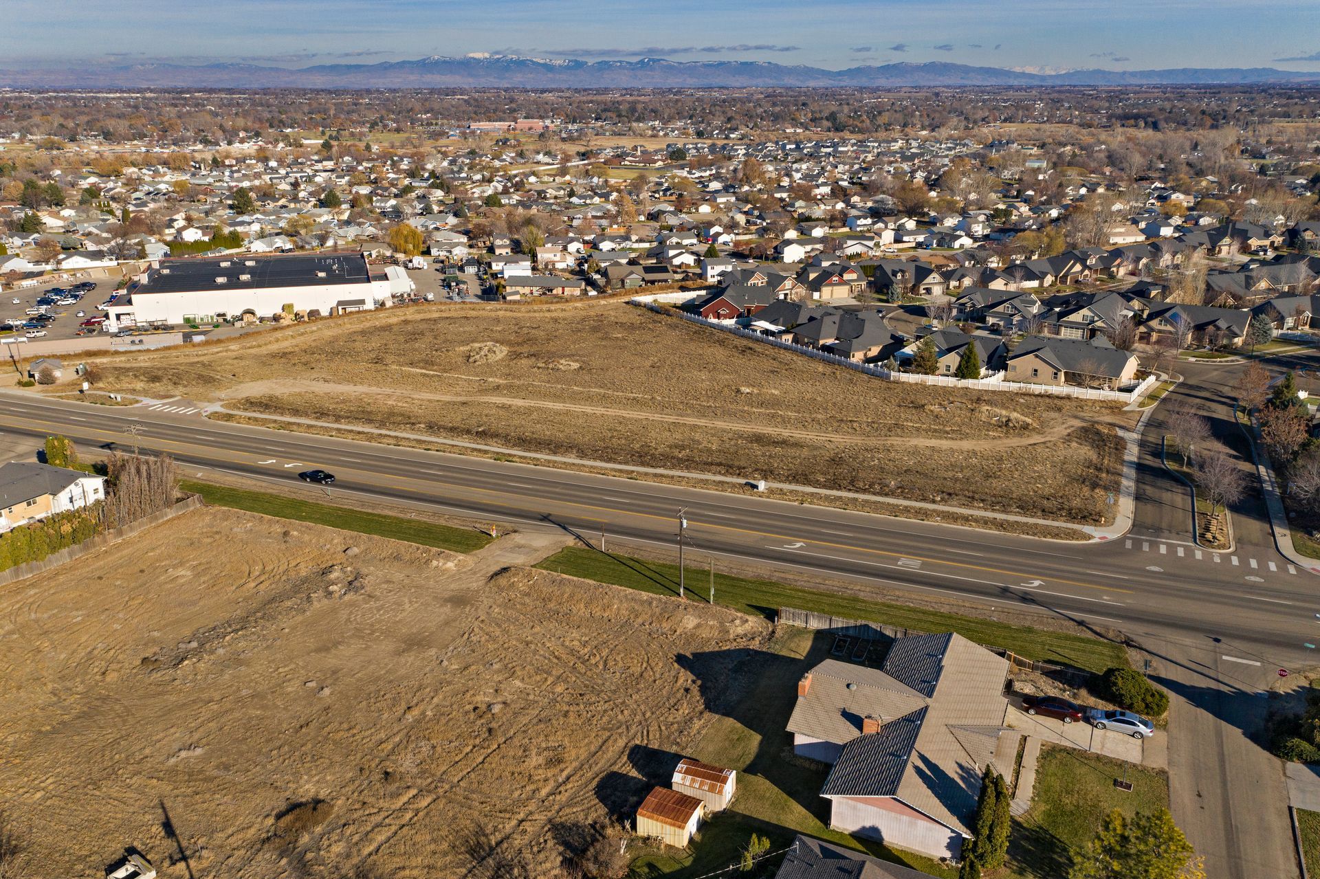 Aerial view of a suburban neighborhood with empty lots and a road under a clear sky.