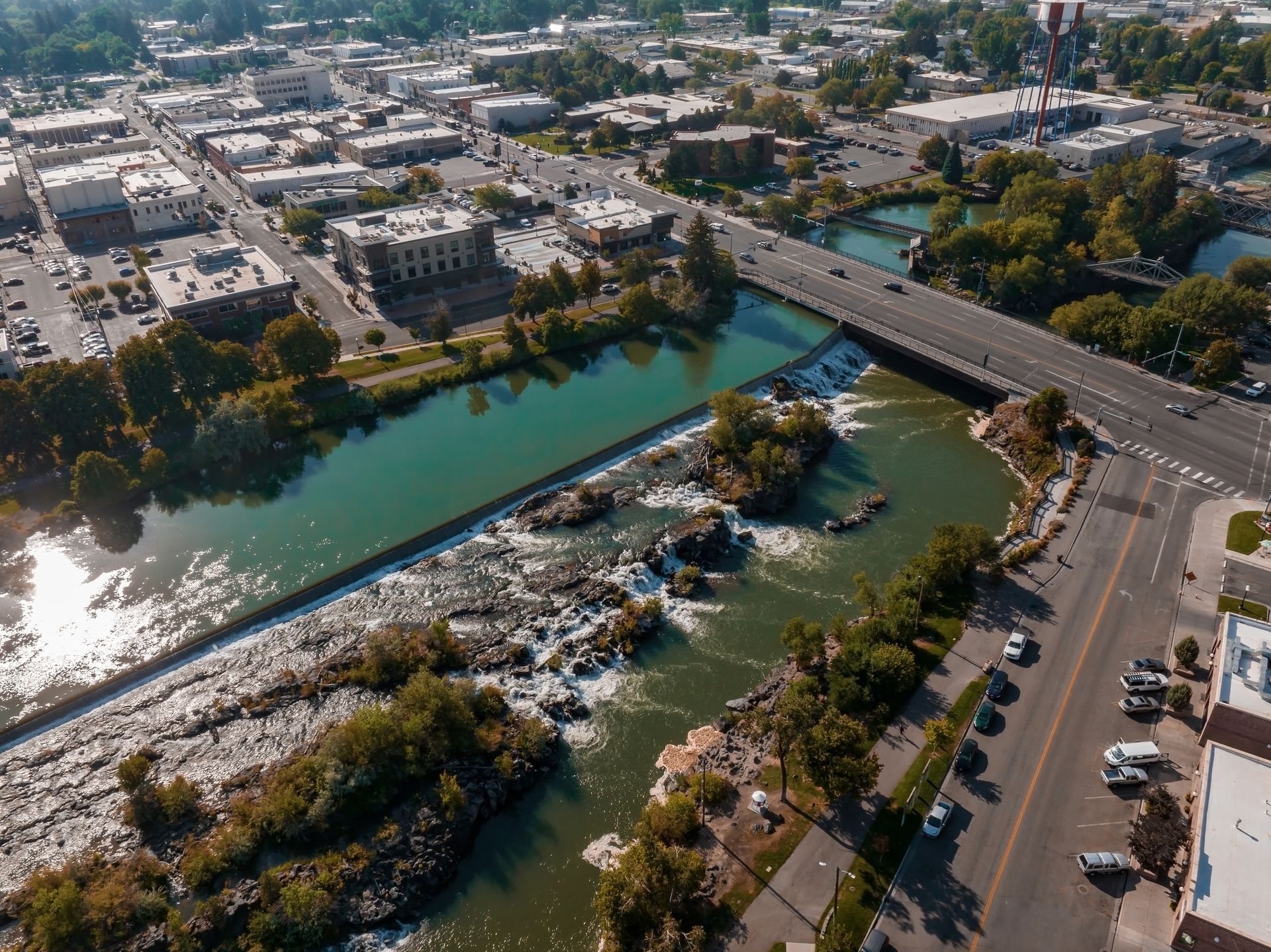 Aerial view of a bridge over a turquoise river beside buildings and streets in a city.