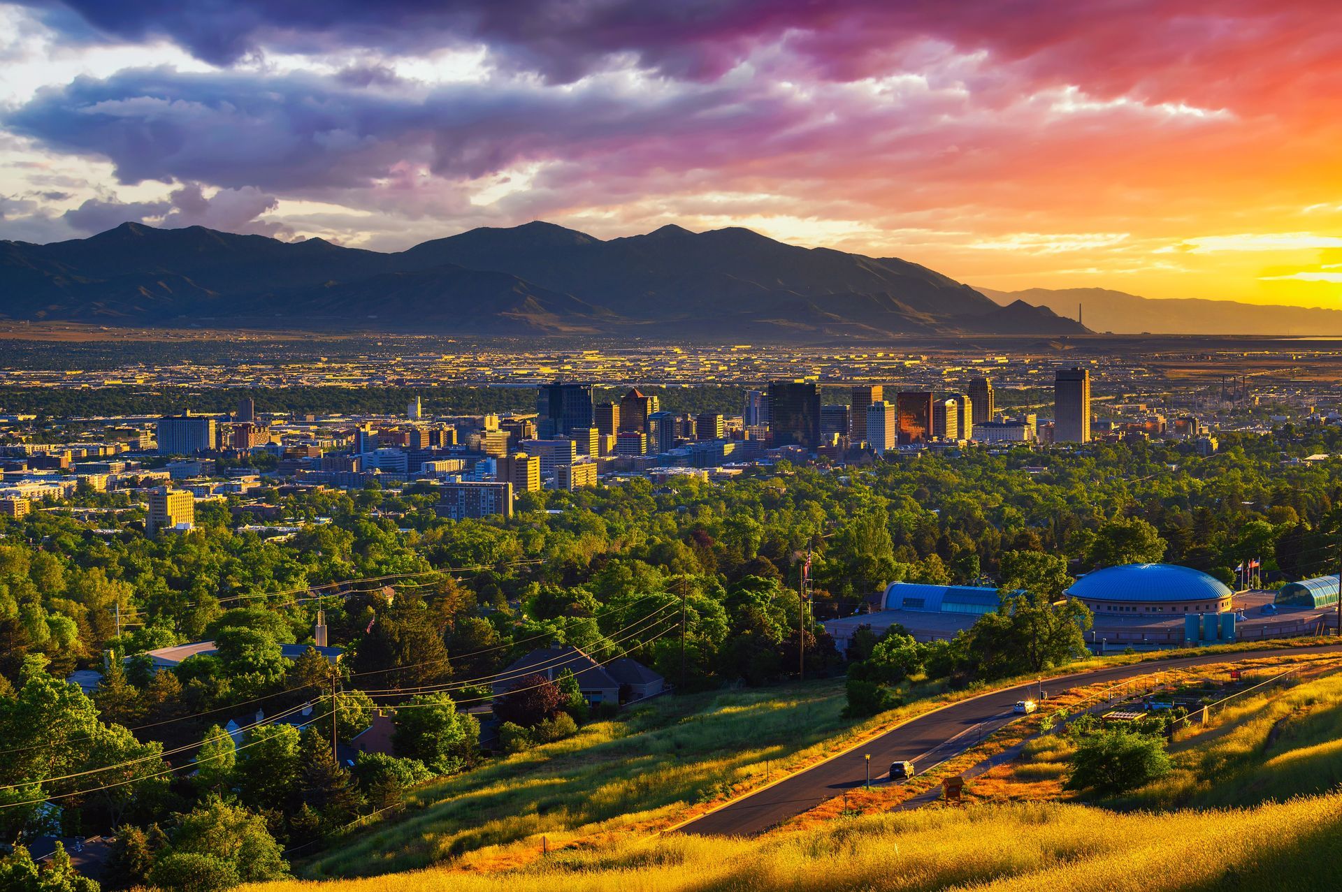 Sunset cityscape with mountains, green hills, and glowing skyline under an orange sky