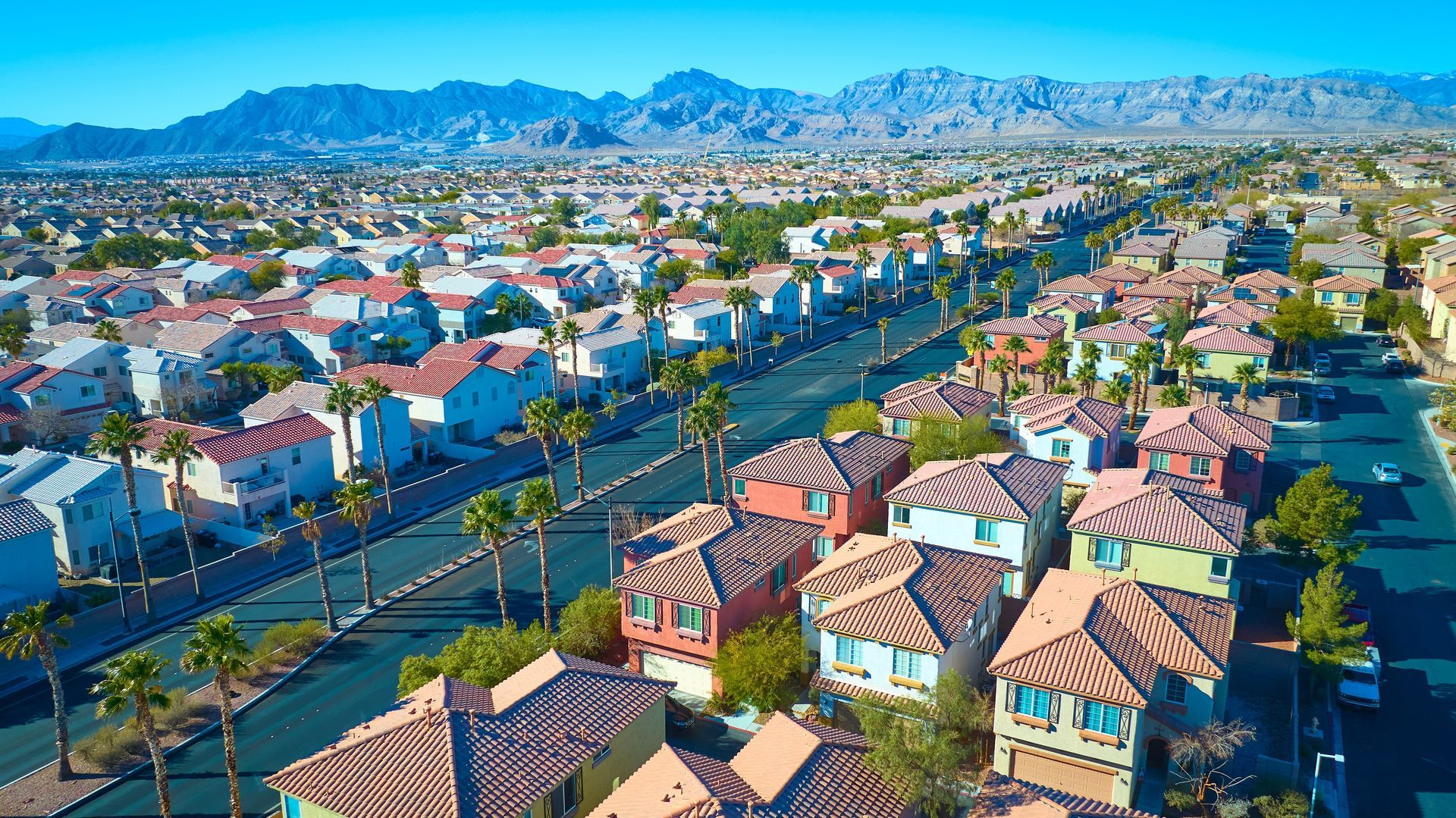 Aerial view of a suburban neighborhood with tiled rooftops, tree-lined streets, and mountains in the distance