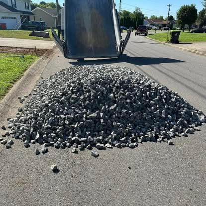 A pile of black gravel spilled on a residential street from an open dump truck.