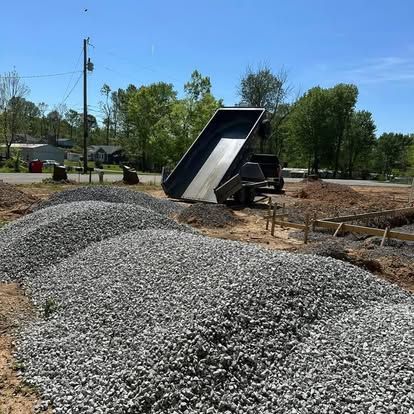 Dump truck unloading gravel at a construction site with gravel piles and trees in the background