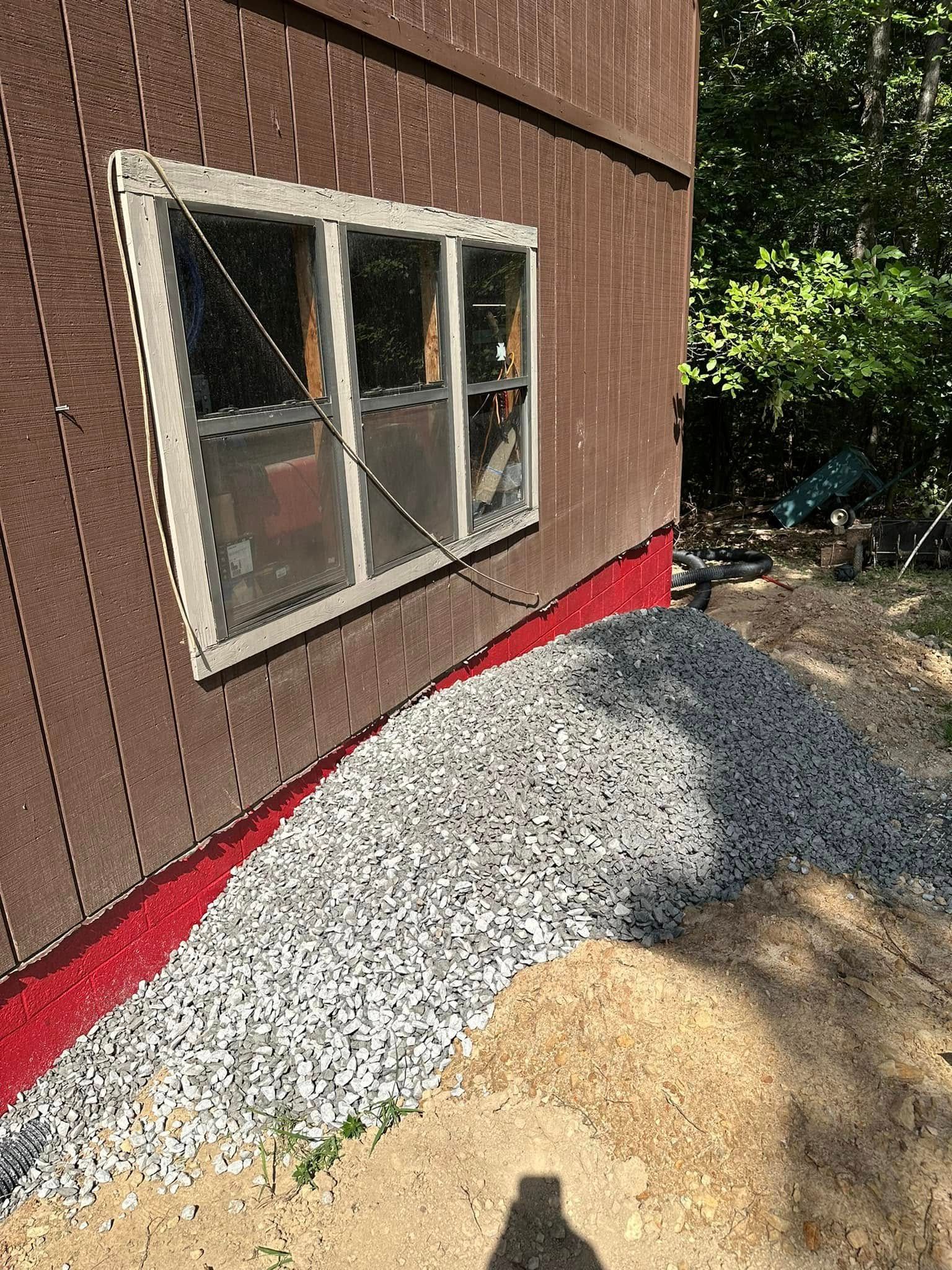 House exterior with window, red foundation trim, and gravel landscaping beside a dirt path.