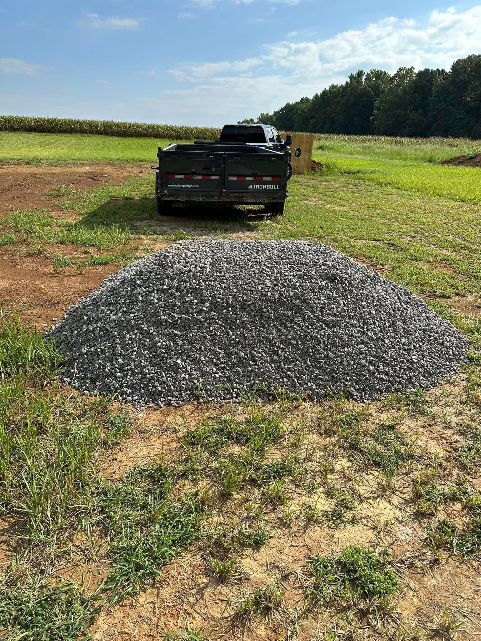 Black truck behind a gravel pile in a grassy field with trees in the background