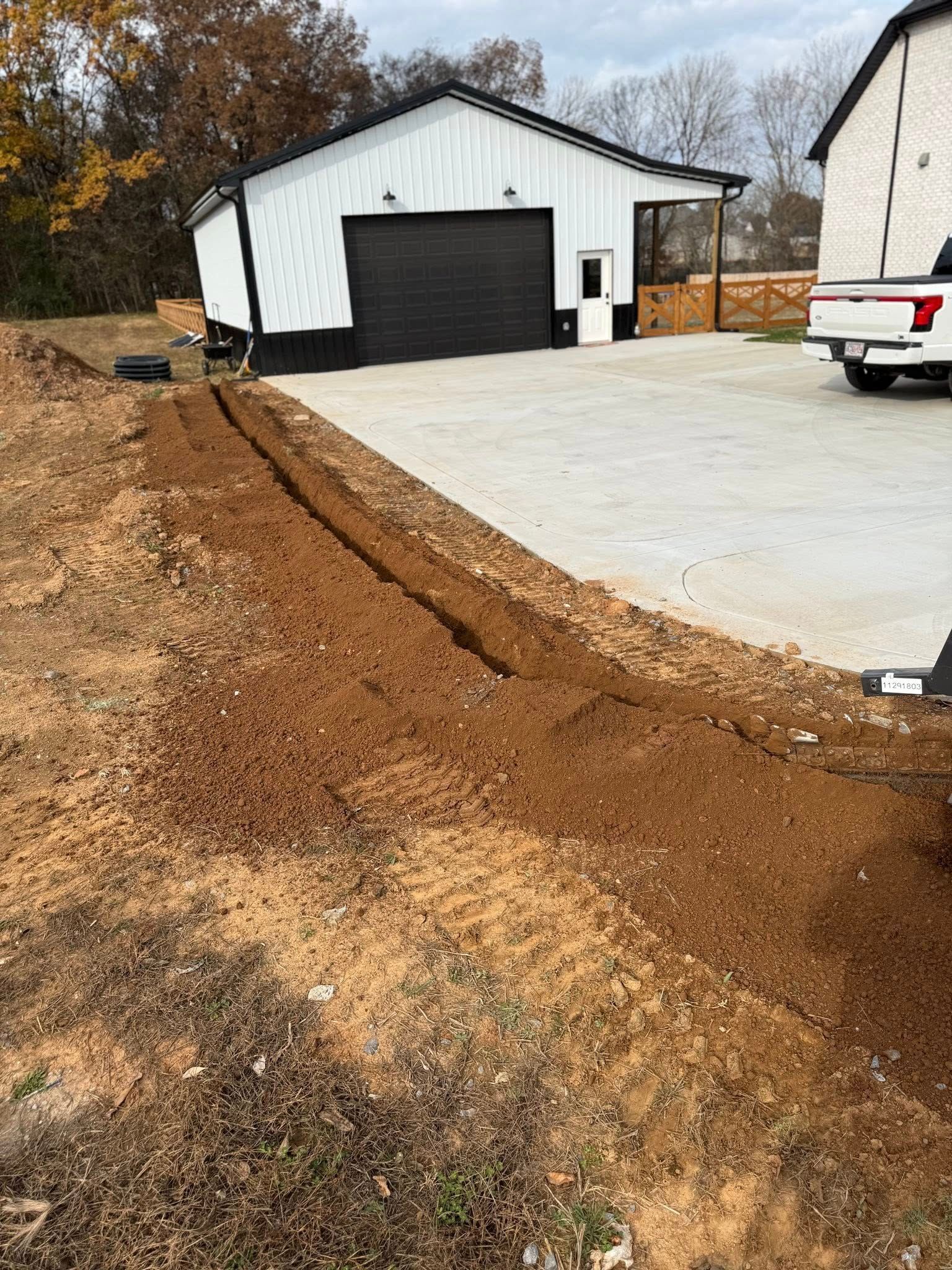 Freshly paved driveway beside a white garage, with a dirt embankment and a parked pickup truck.