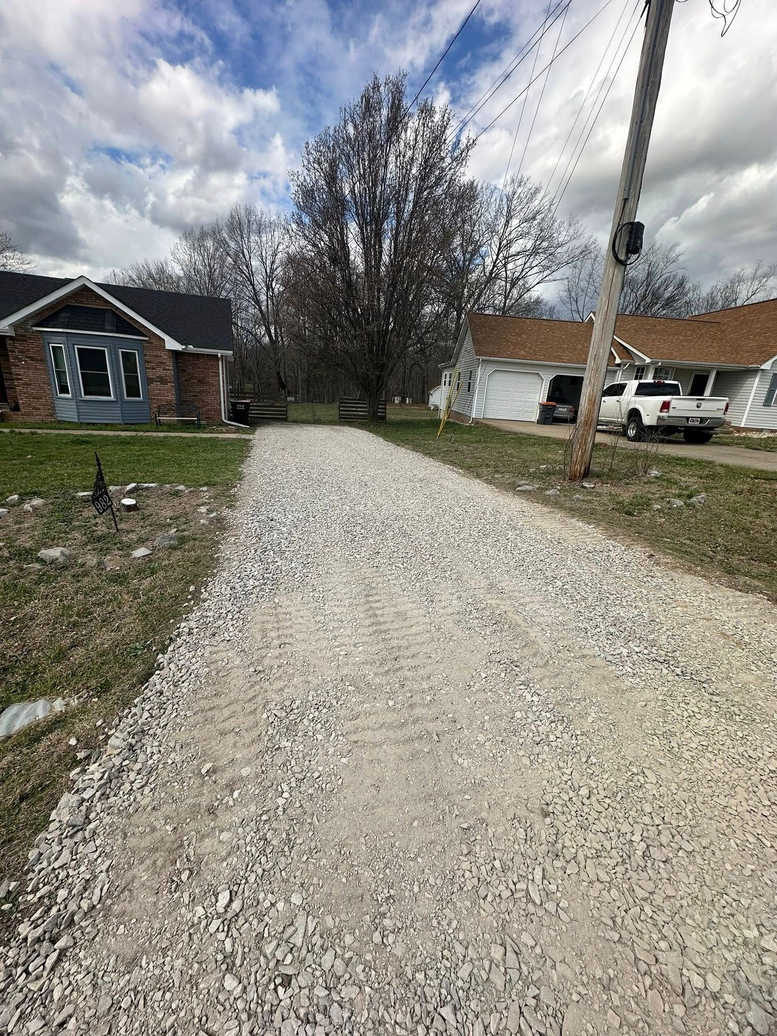 Gravel driveway leading to houses on a cloudy suburban street with parked vehicles