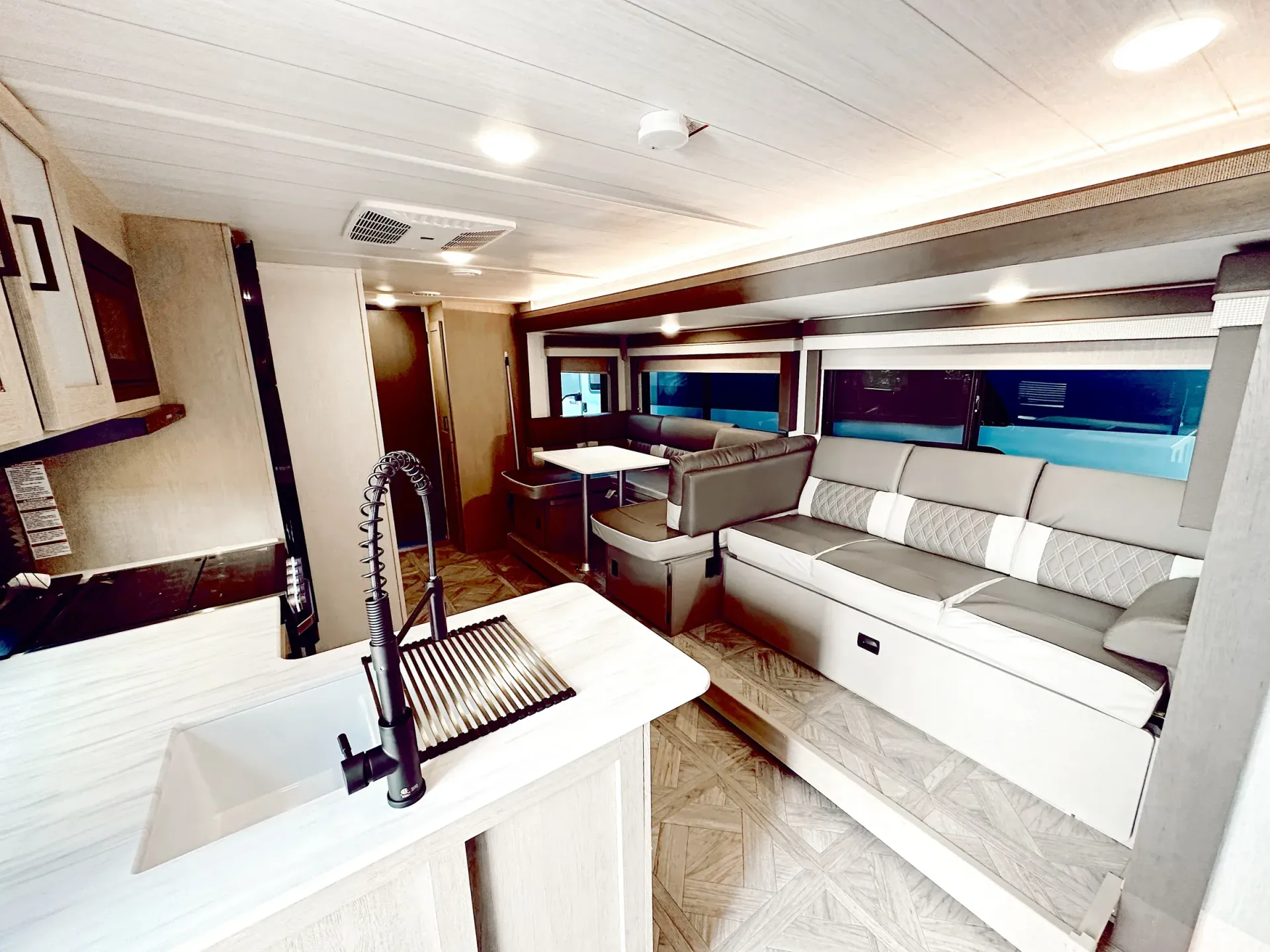 Modern RV interior with white benches, a table, and bunk beds in a compact living space