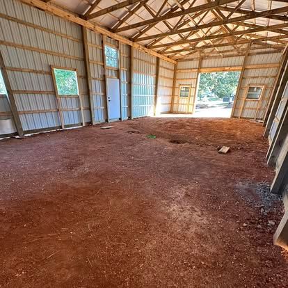 Empty metal barn interior with dirt floor, open doorway, and sunlight streaming in