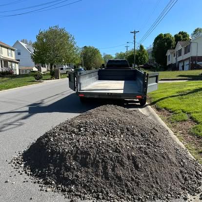 Trailer parked behind a large gravel pile on a sunny suburban street