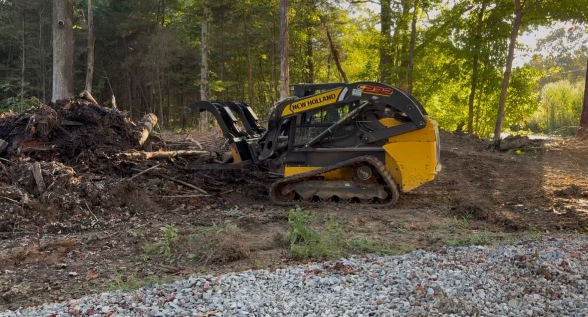 Yellow-and-black skid steer stuck in a muddy wooded area, surrounded by dirt piles and trees