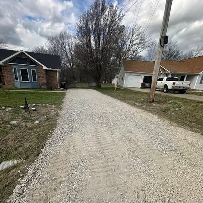 Gravel driveway between brick house and white garage in a suburban neighborhood under cloudy skies