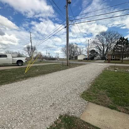 Gravel driveway beside utility poles, a white truck, and houses under a cloudy sky