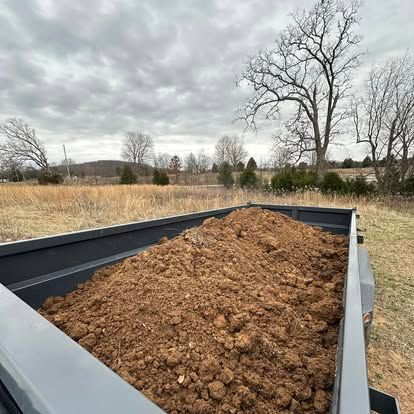 Dump trailer filled with brown dirt in a cloudy rural field