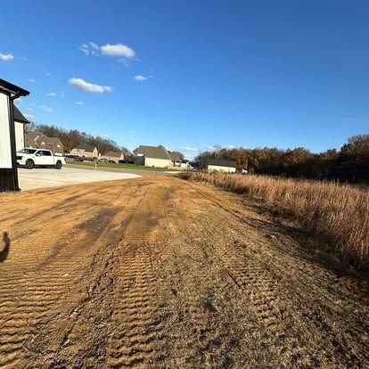 Graded dirt lot beside houses under a clear blue sky with a parked white truck