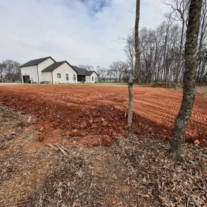 New white house under construction beside red dirt and leafless trees on a rural lot