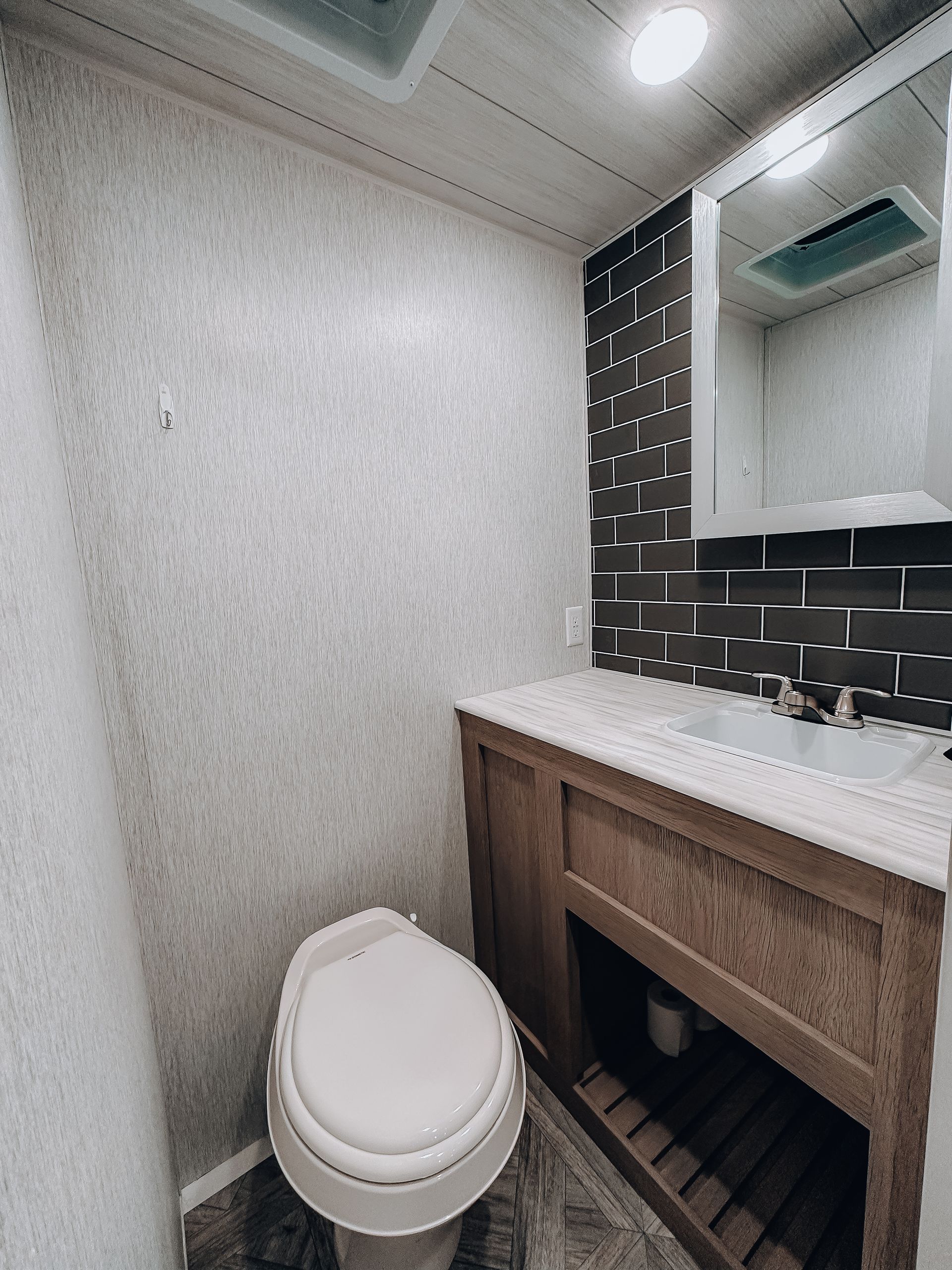 Small bathroom with toilet, wood vanity, white countertop, and tiled mirror wall.