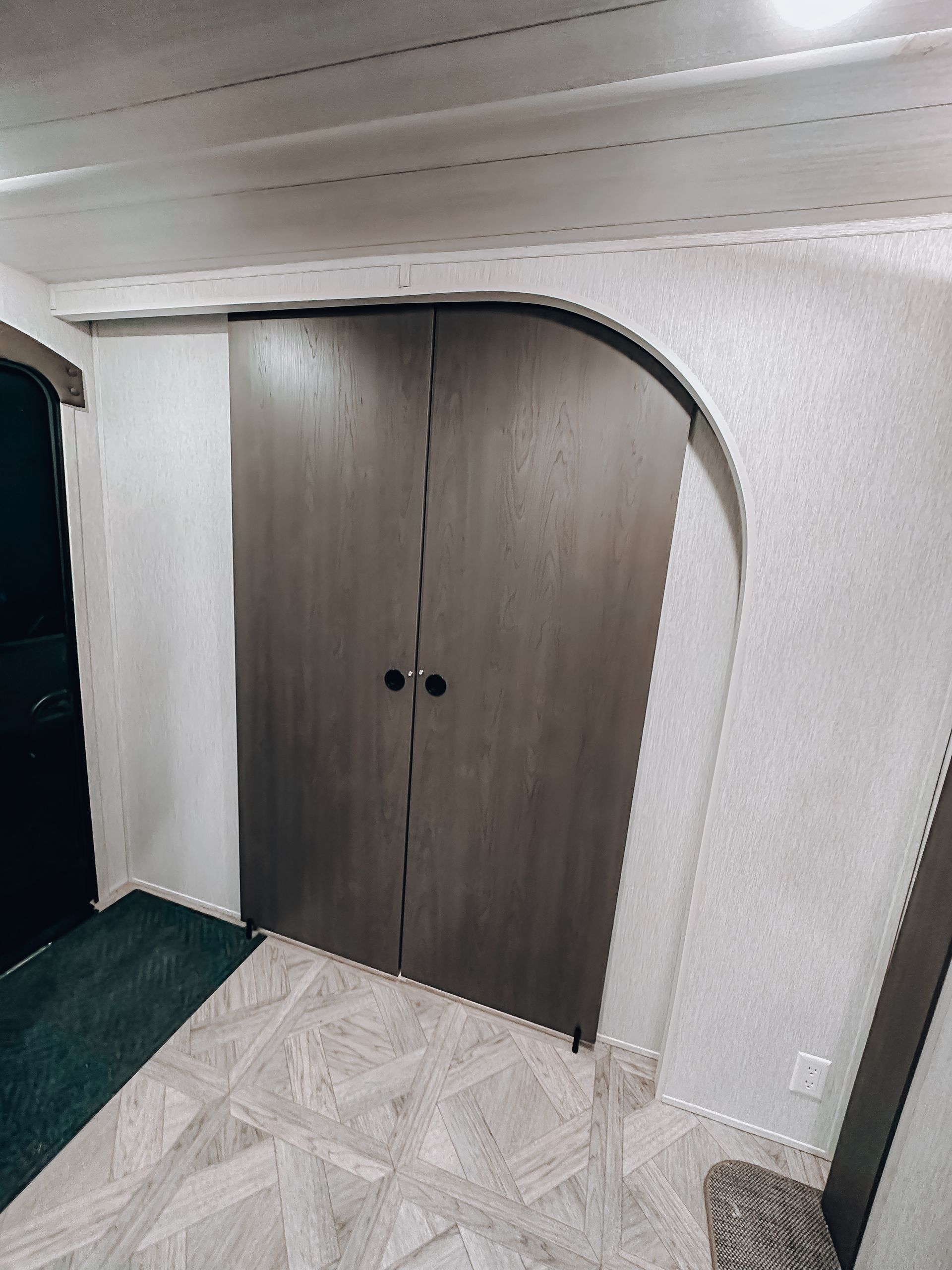 White arched wall with dark wooden double doors in a small interior room with patterned tile flooring