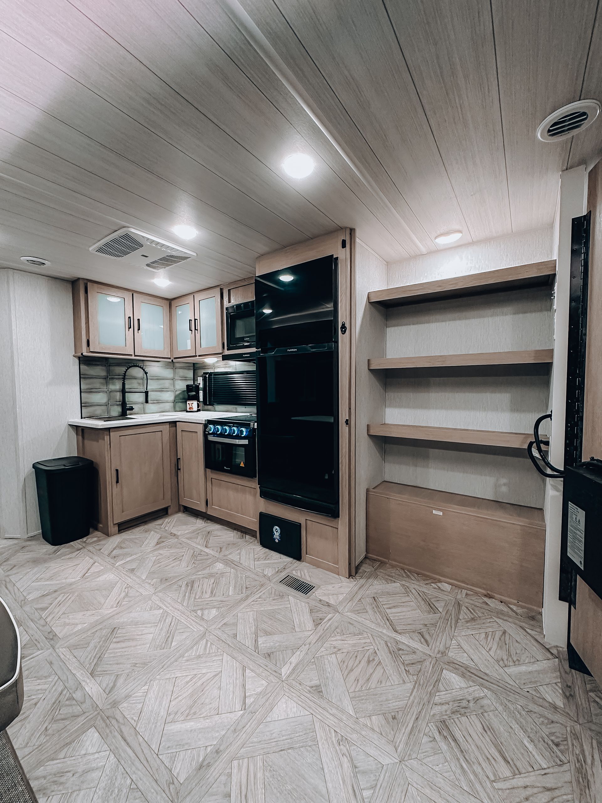 Small kitchen interior with wood cabinets, black appliances, and open shelving on the right.