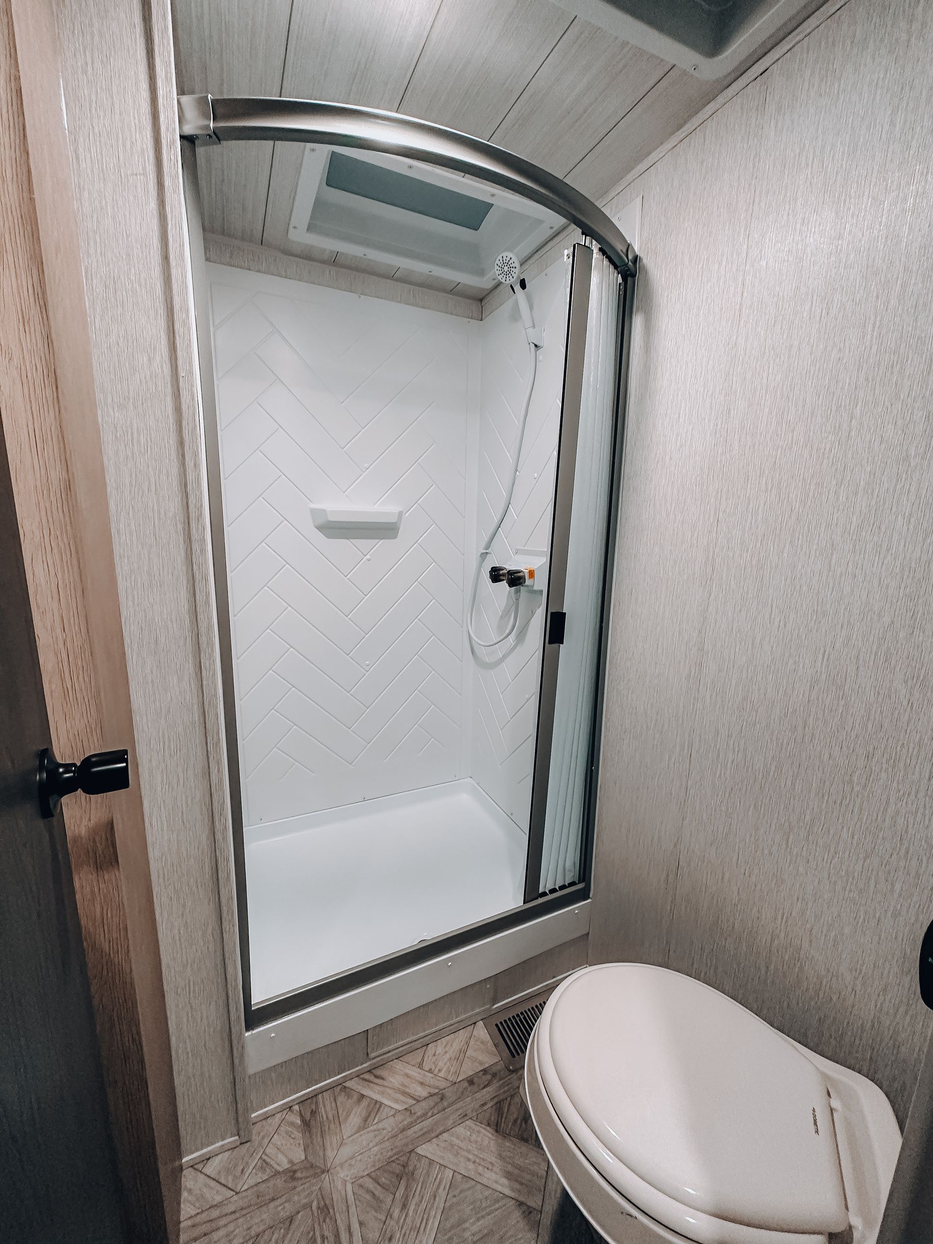 Compact bathroom with glass shower stall, tiled walls, and toilet in foreground.