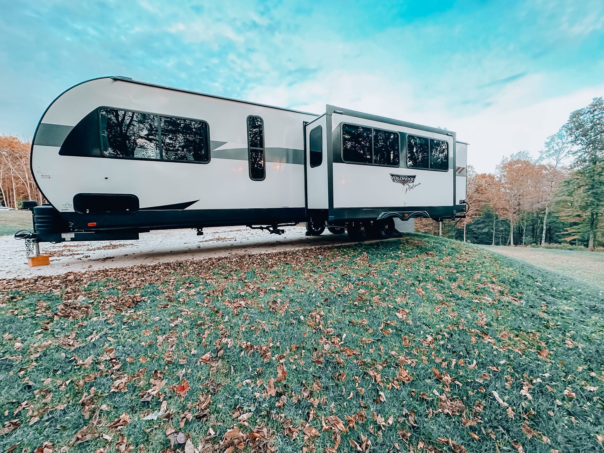 White travel trailer parked on a grassy hill with autumn trees in the background
