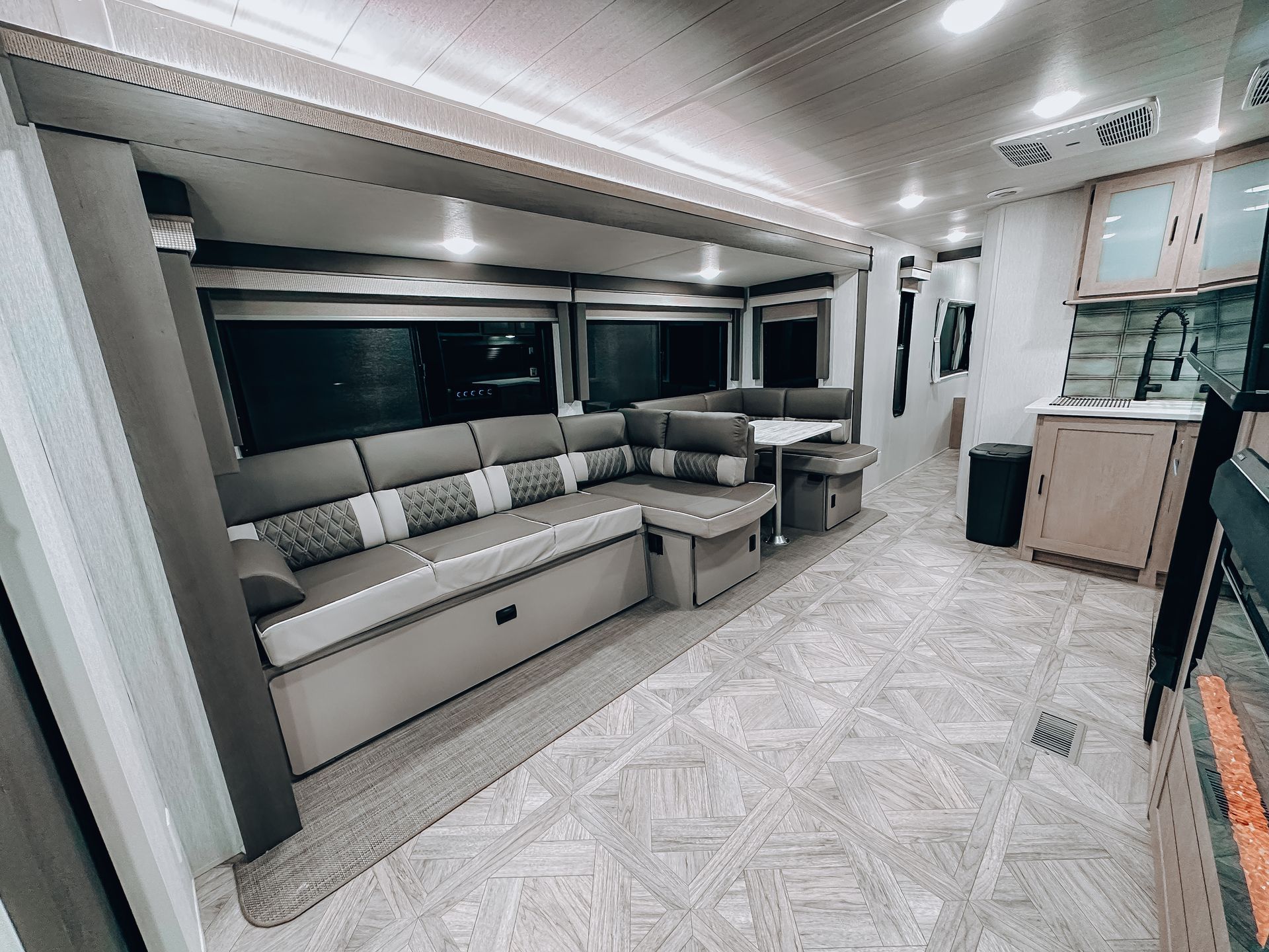 Modern RV interior with a gray L-shaped sofa, white cabinetry, and bright floor space
