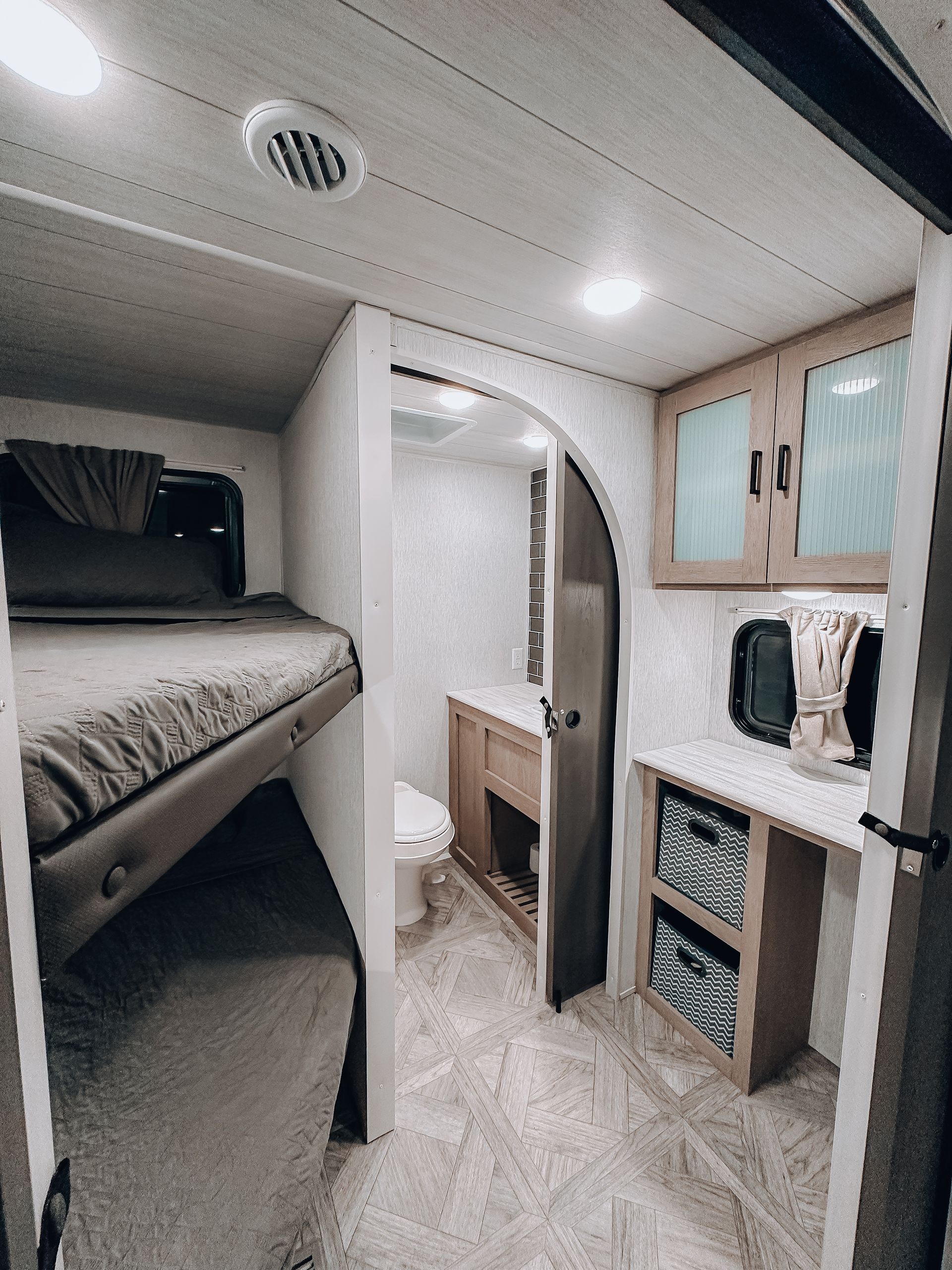 Compact RV interior with bunk beds, small sink, and cabinets in light wood and white.