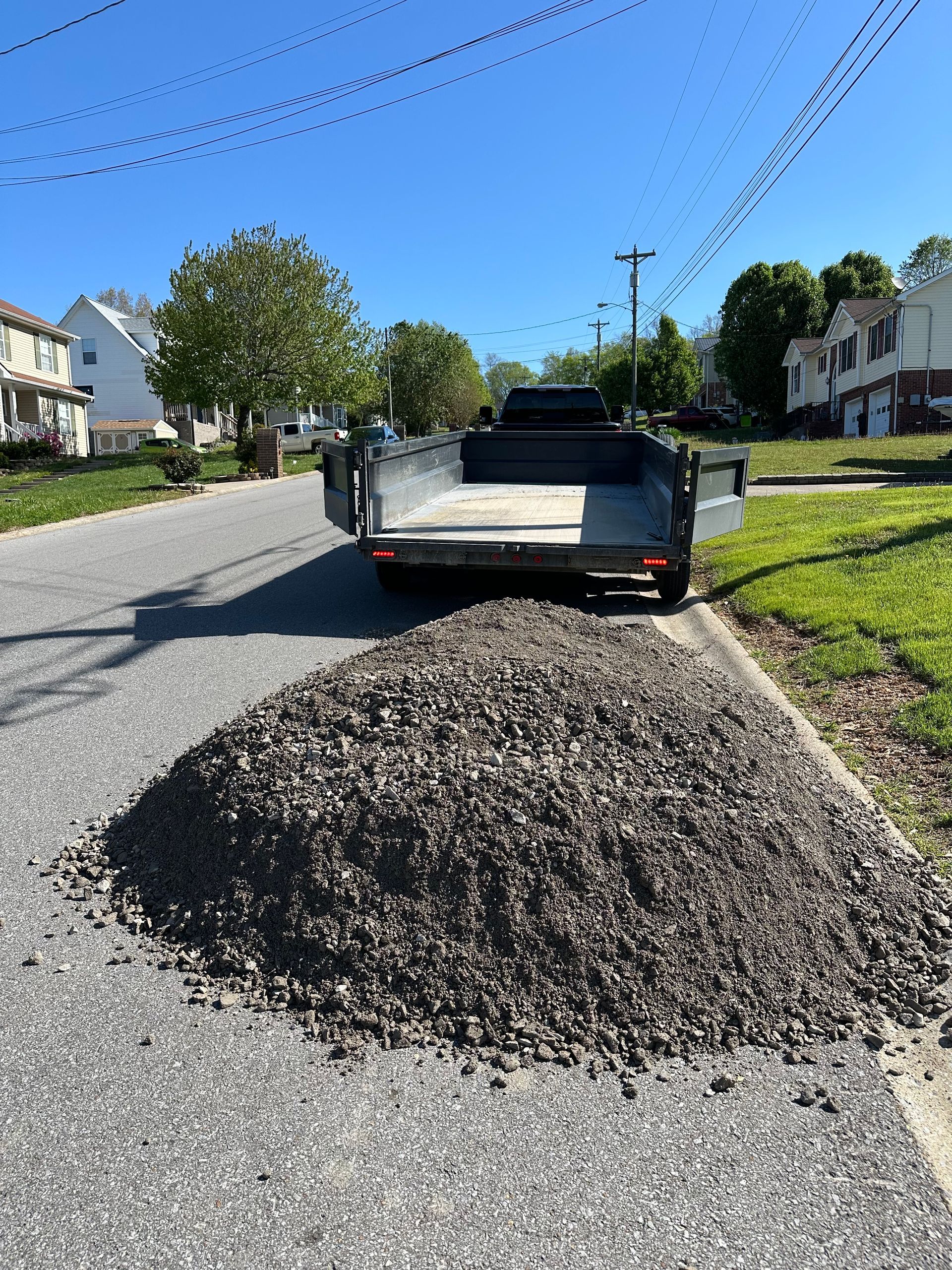 Pickup truck unloading gravel onto a residential street beside houses and lawns