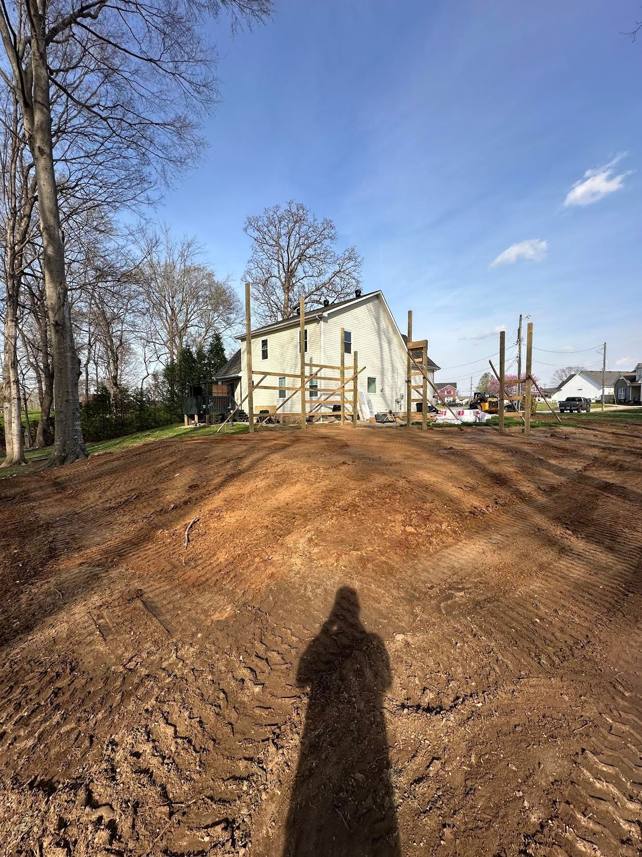 Dirt mound in foreground with a house under construction on a sunny day, trees and blue sky behind.