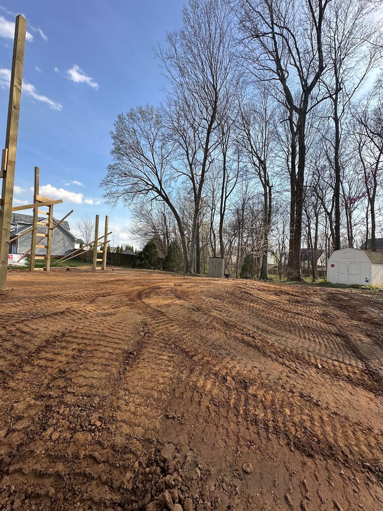 Dirt road through a cleared lot with utility poles and bare trees under a blue sky