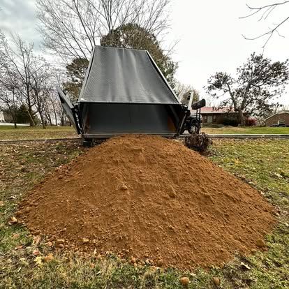 Small tractor dumping a large pile of brown mulch in a grassy park.