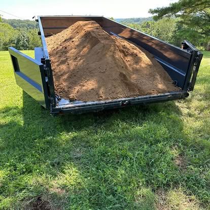 Dump trailer loaded with a large pile of dirt on a grassy field