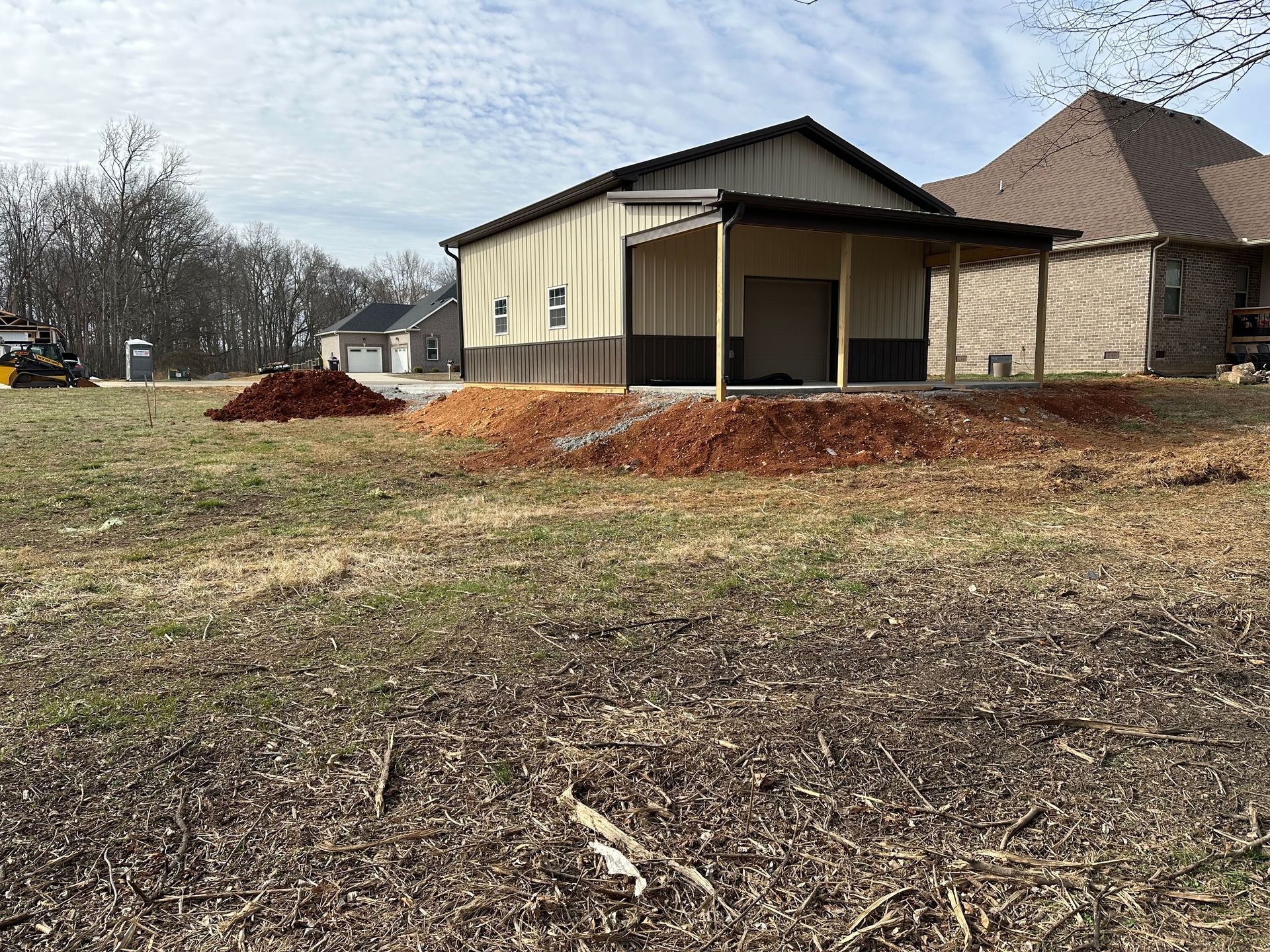 Small beige building with covered porch beside a house, on a grassy lot with mulch in front.