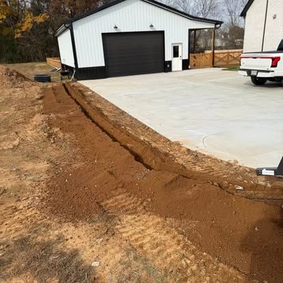 Fresh concrete driveway beside a white metal garage with a black door, next to a dug trench and dirt