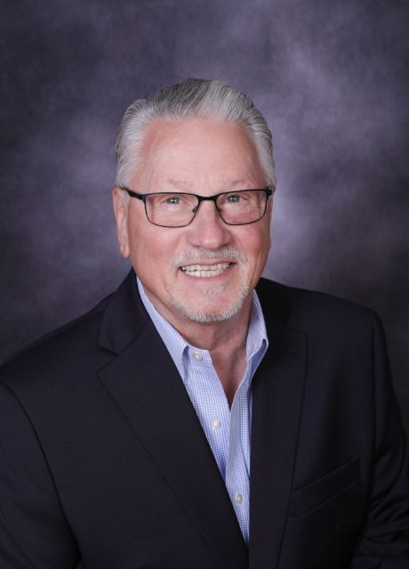 Smiling man in glasses and dark blazer against a gray studio backdrop