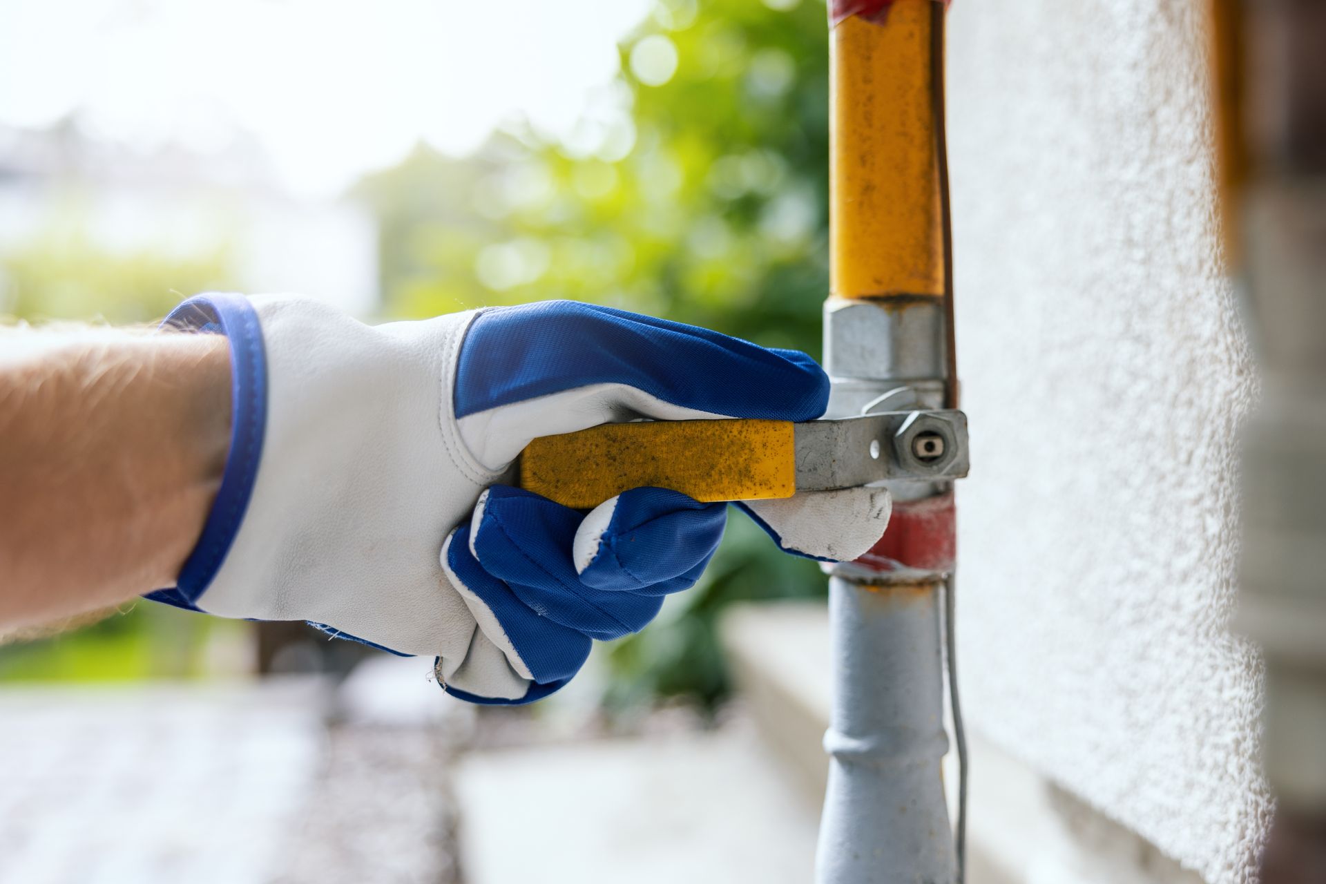 Gloved hand turning a yellow gas valve on a pipe outside a building.