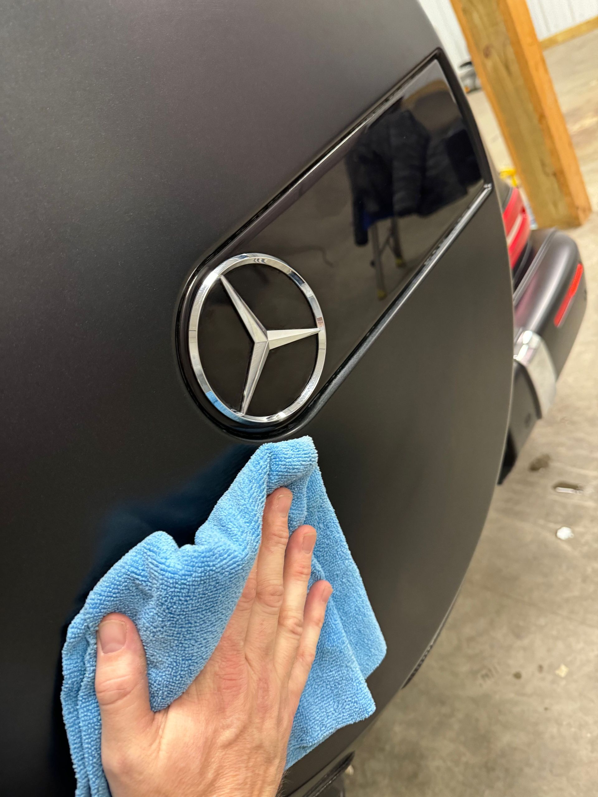A person is cleaning a black mercedes with a blue towel.