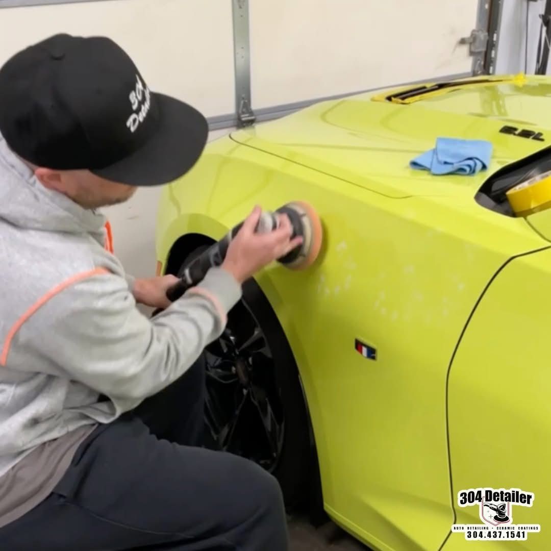 A man wearing a black hat is polishing a yellow car