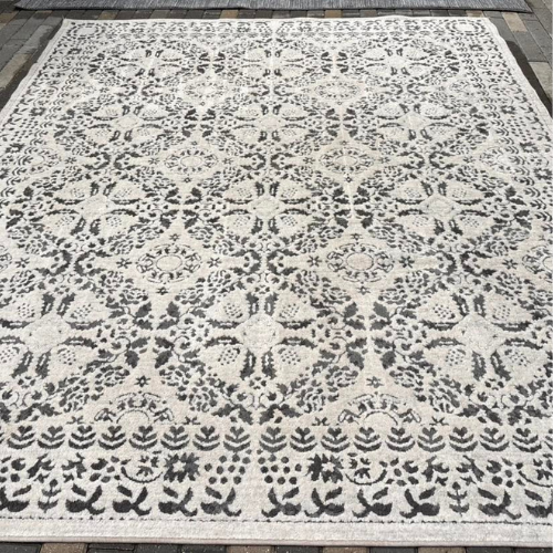 A large, ornate rug with a cream background and dark gray floral pattern.