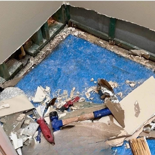 Demolished room corner, blue floor, wood frame, debris, tools present.