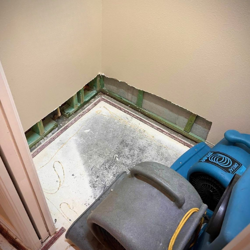 A corner of a room with exposed framing, concrete floor, and drying equipment, possibly water damage.