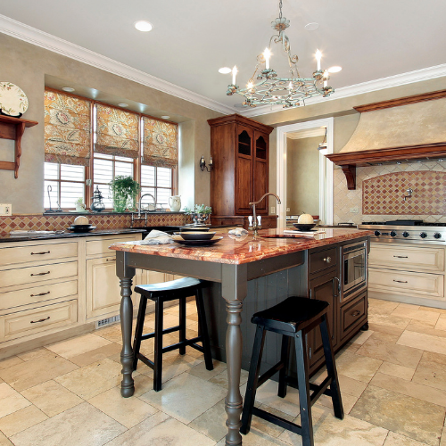 Elegant kitchen with island, wooden cabinets, and a chandelier. Beige walls and stone flooring.