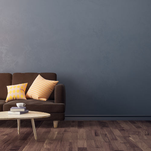 Brown sofa with orange and yellow pillows, round table with books, dark blue wall, wooden floor.