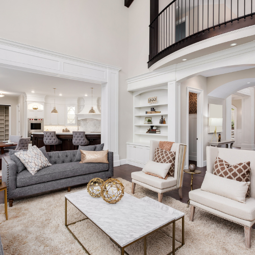 Spacious living room with gray sofa, white armchairs, marble coffee table, and view to kitchen.