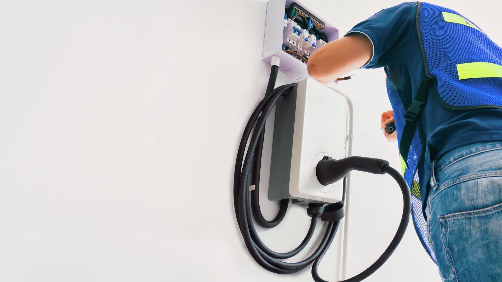 Electrician installing a white EV charger on a wall.