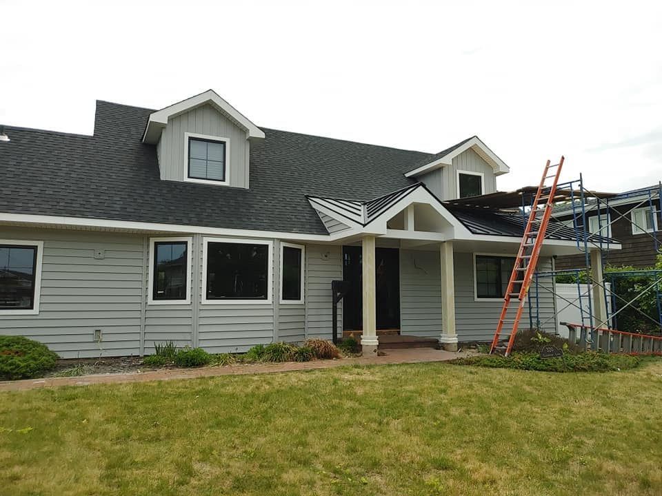 Gray house with a dark roof and dormers, ladder leaning against the side.